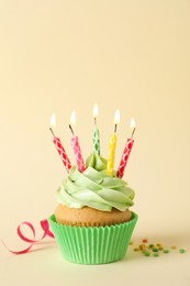 Photo of Birthday cupcake with burning candles, streamer and sprinkles on beige background