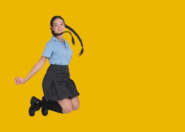 Happy girl in school uniform jumping on golden background, space for text