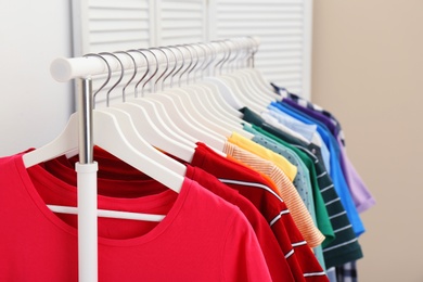 Photo of Rack with bright clothes in room. Rainbow colors