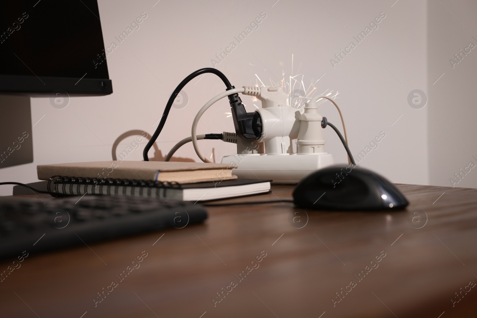 Photo of Inflamed plug in power strip indoors on wooden table. Electrical short circuit