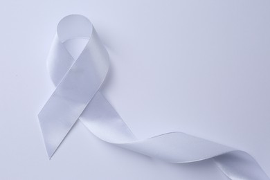 Photo of White awareness ribbon on white background, top view