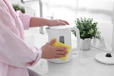 Woman cleaning electric kettle with sponge at countertop in kitchen, closeup
