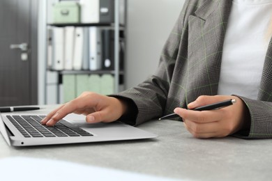 Photo of Woman working with laptop and holding pen at table indoors, closeup