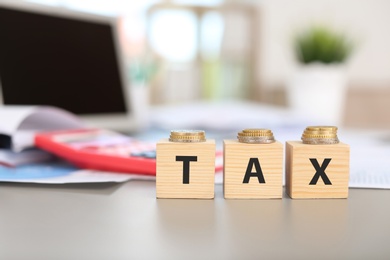 Wooden cubes with word TAX and coins on table