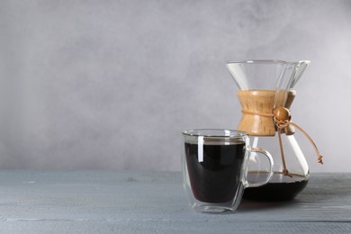 Photo of Chemex coffeemaker and glass with tasty drip coffee on grey wooden table. Space for text