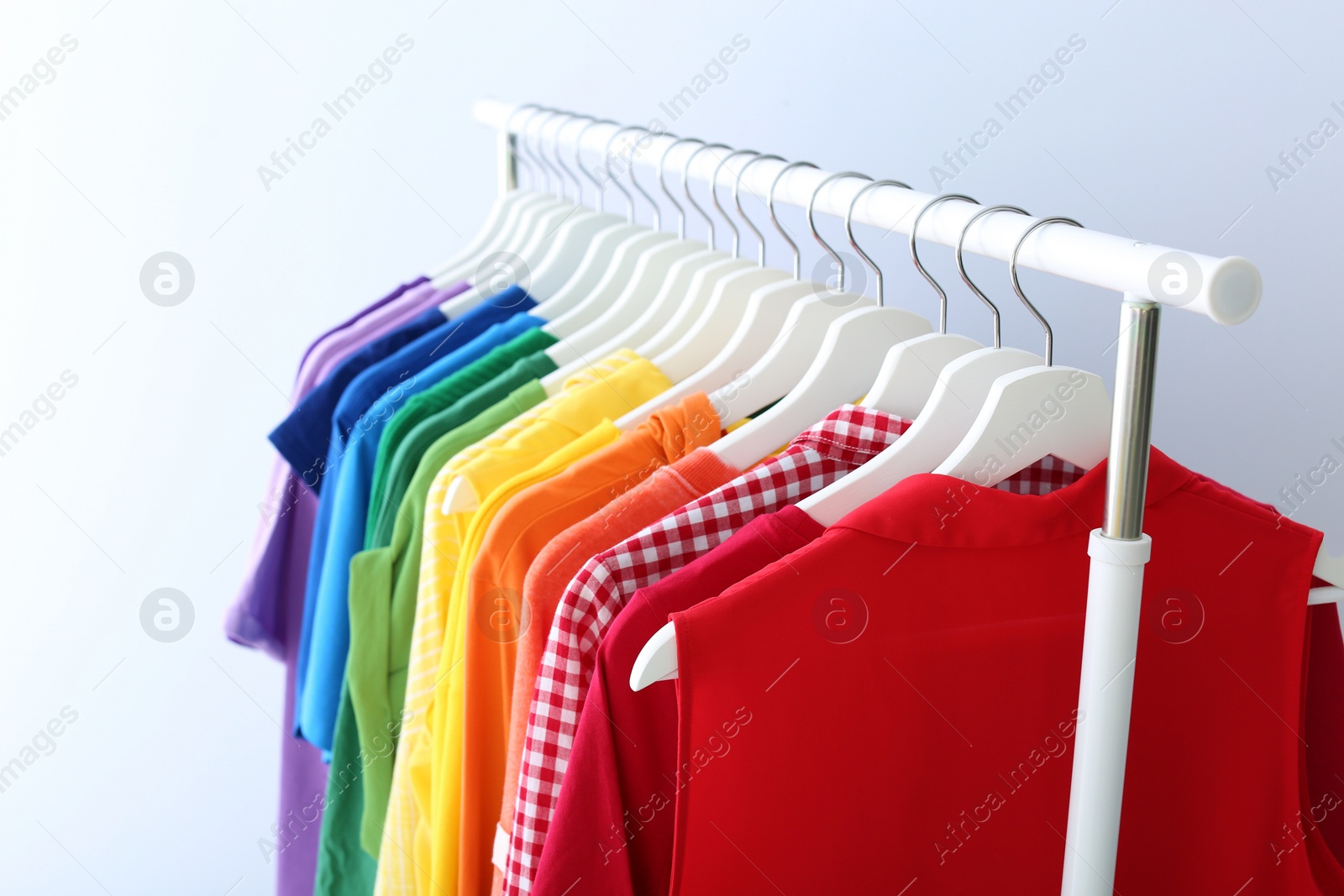 Photo of Rack with rainbow clothes on light background