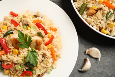 Photo of Delicious rice pilaf with chicken and vegetables on black table, closeup