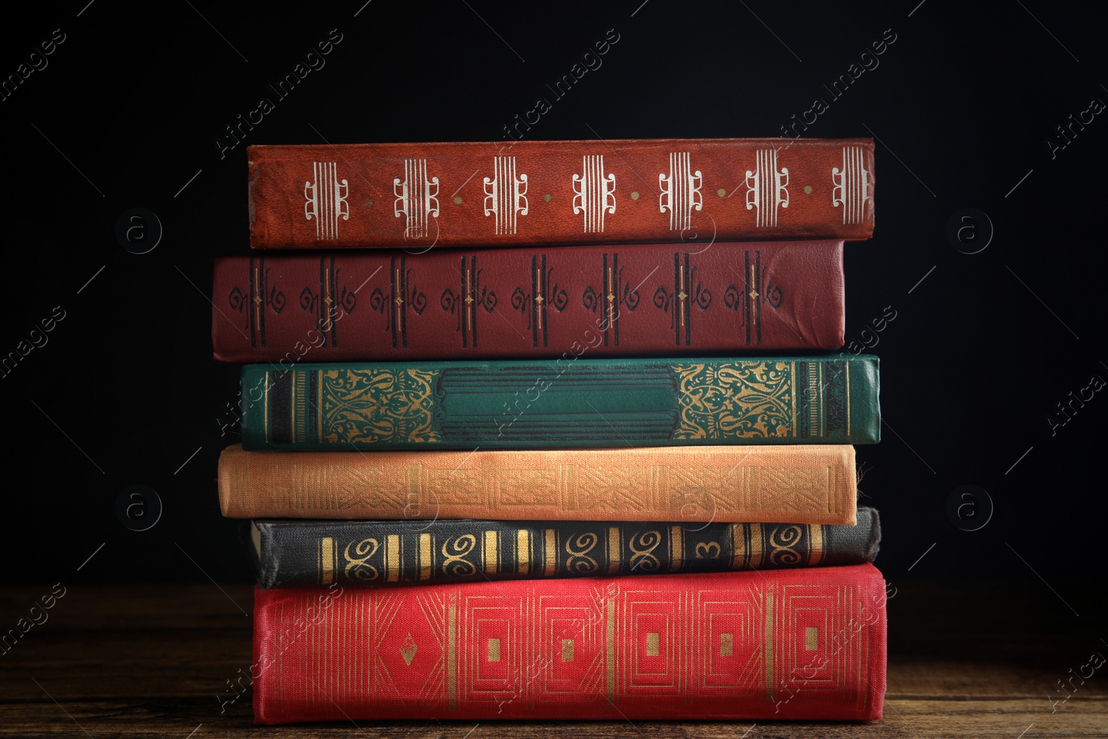 Photo of Collection of different books on wooden table against dark background