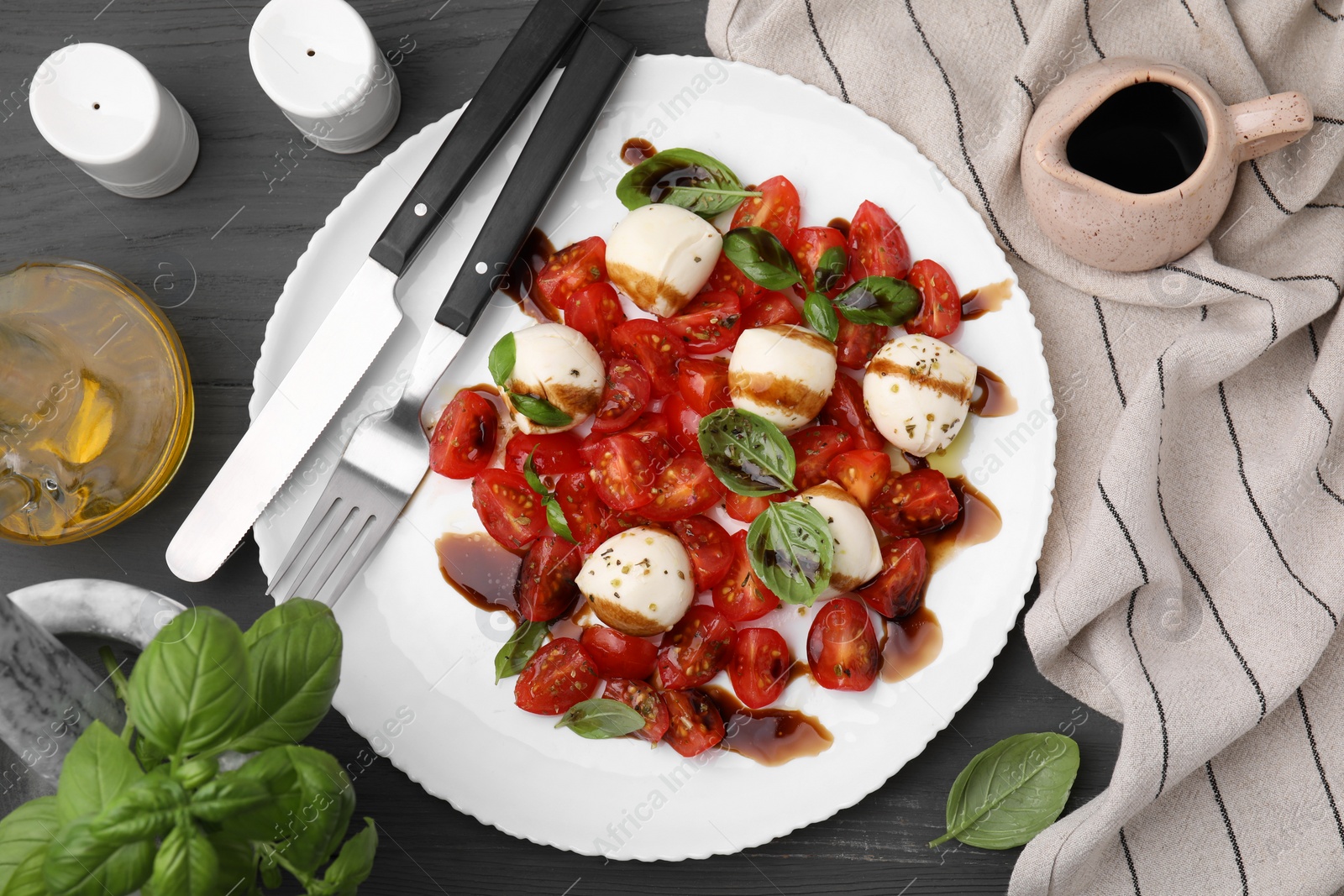 Photo of Tasty salad Caprese with tomatoes, mozzarella balls, basil served on grey wooden table, flat lay