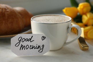 Photo of Cup of coffee, croissant and card with phrase GOOD MORNING on white tray, closeup