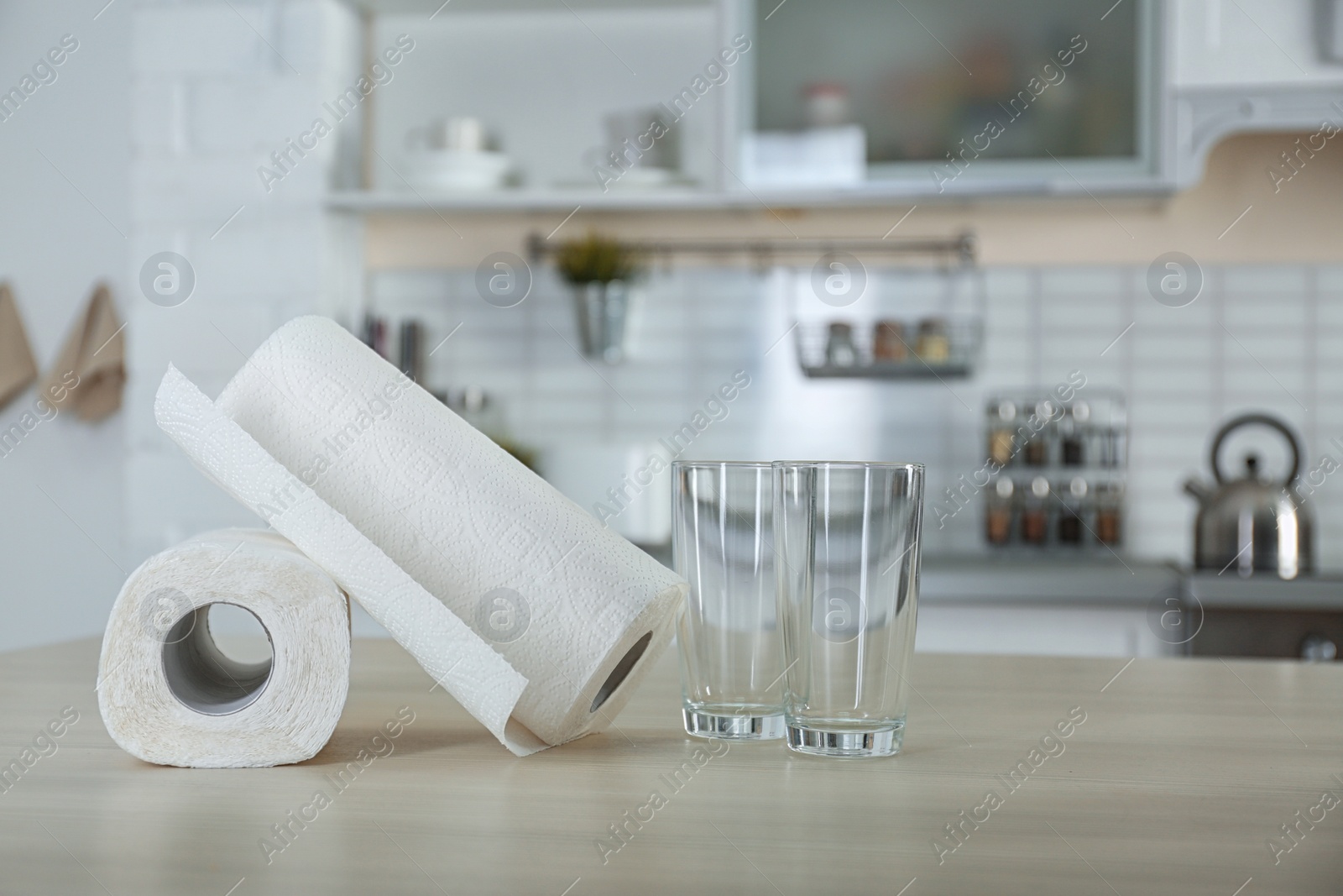 Photo of Rolls of paper towels and glasses on table in kitchen. Space for text