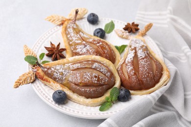 Delicious pears baked in puff pastry with powdered sugar on light table, closeup