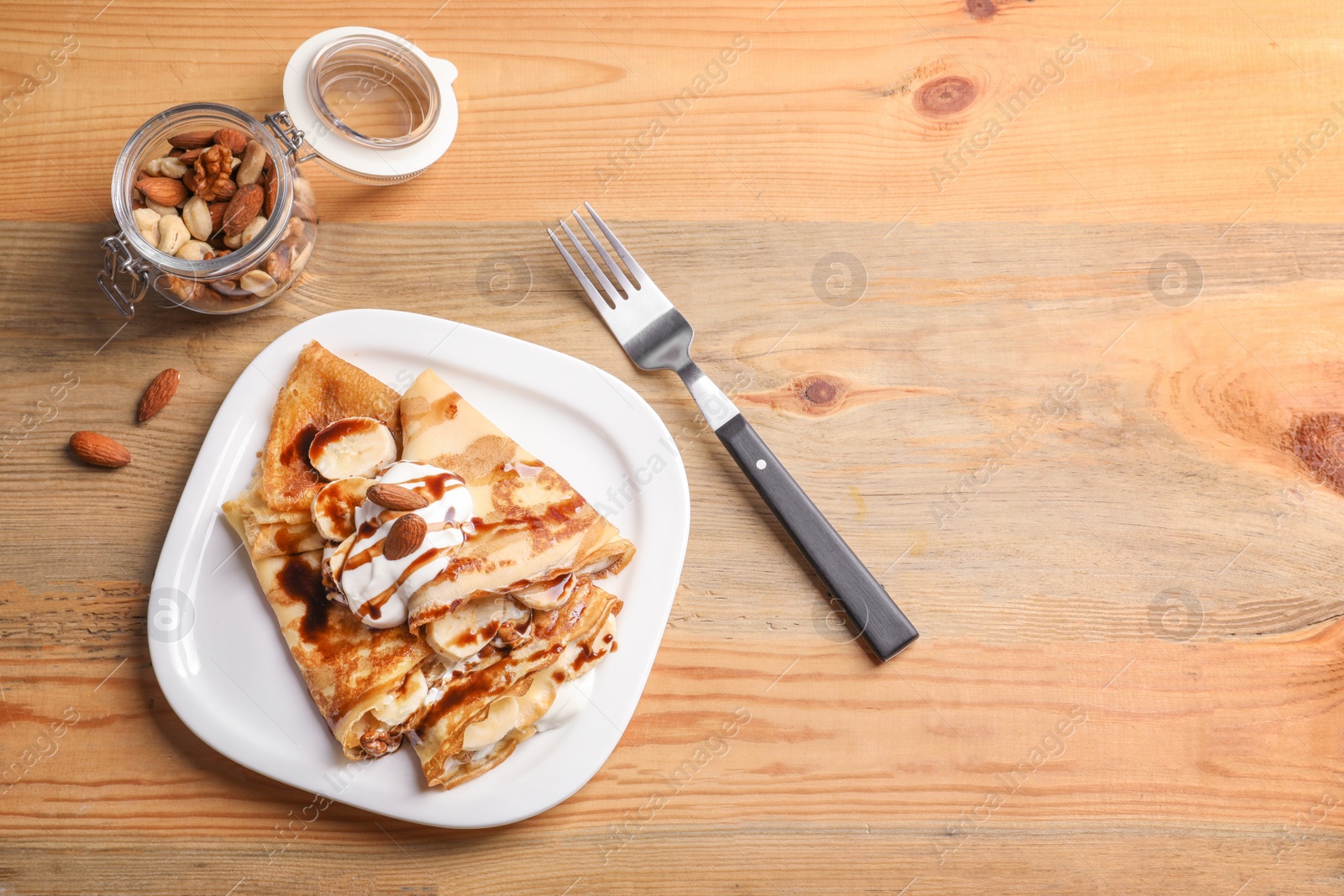 Photo of Thin pancakes served with chocolate syrup, cream and banana on plate, top view