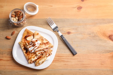 Photo of Thin pancakes served with chocolate syrup, cream and banana on plate, top view