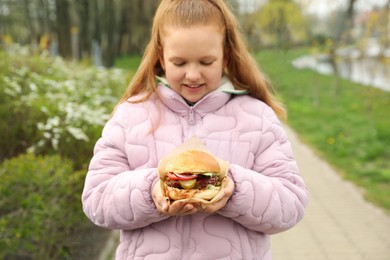 Photo of Little girl holding fresh delicious burger outdoors. Street food