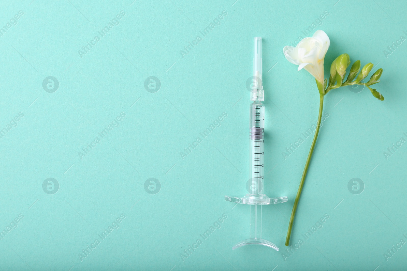 Photo of Cosmetology. Medical syringe and freesia flower on turquoise background, top view. Space for text