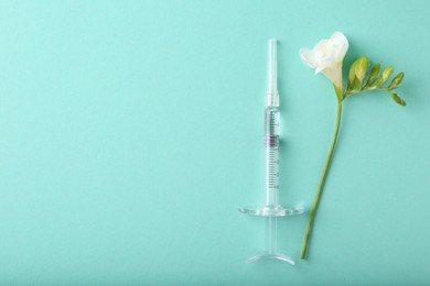 Photo of Cosmetology. Medical syringe and freesia flower on turquoise background, top view. Space for text