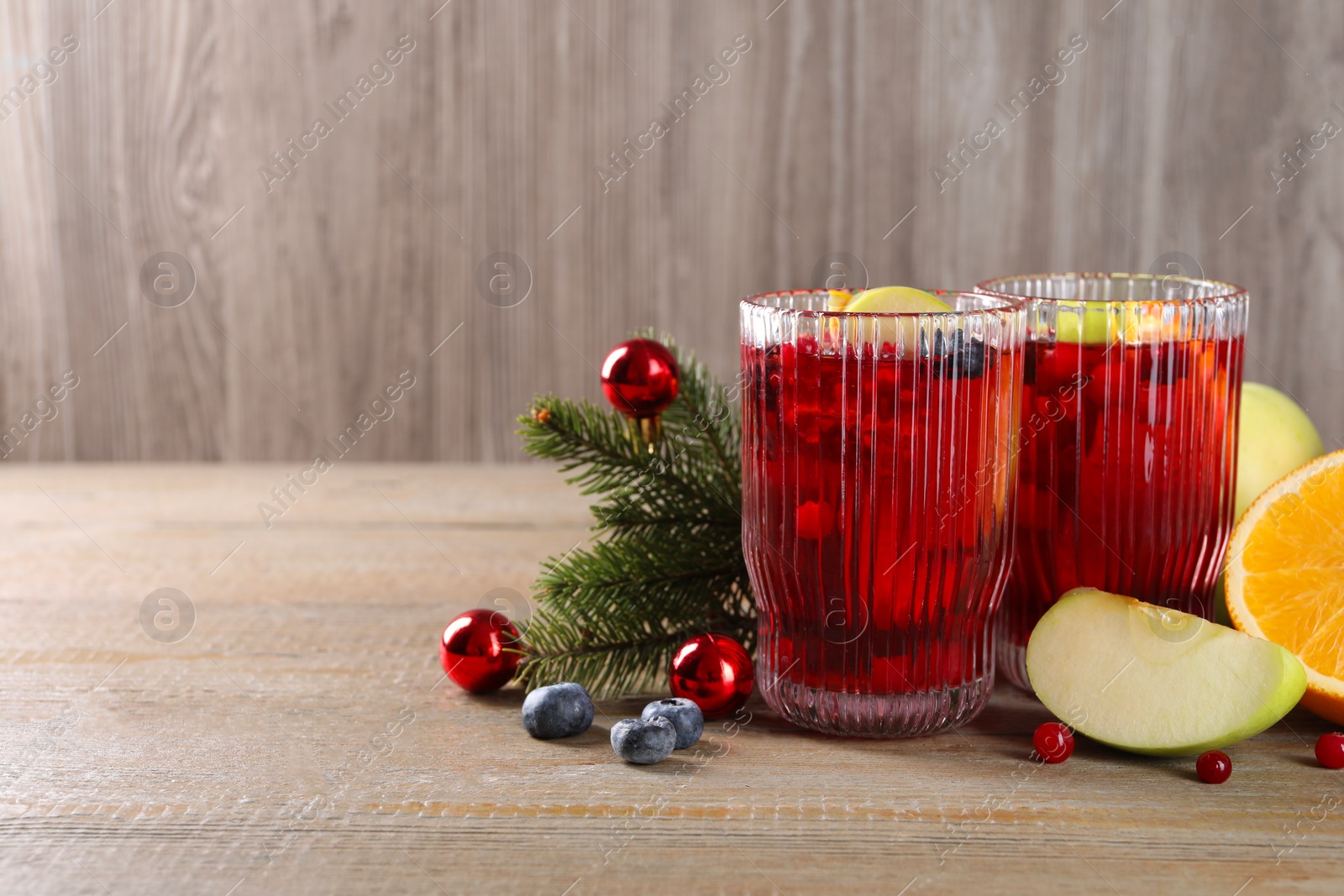 Photo of Aromatic Sangria drink in glasses, ingredients and Christmas decor on wooden table. Space for text
