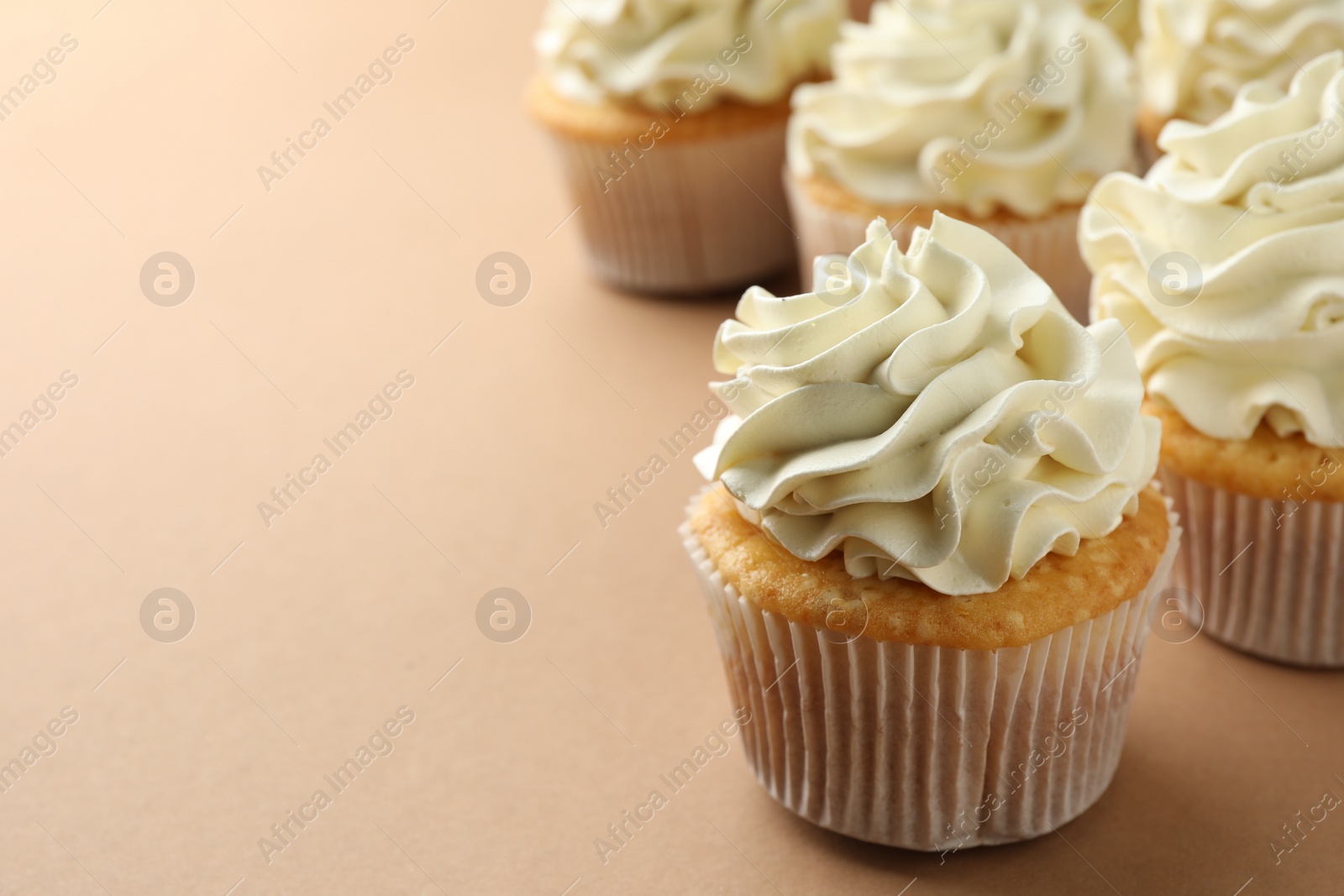 Photo of Tasty vanilla cupcakes with cream on beige table, closeup. Space for text