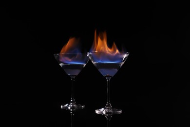 Photo of Cocktail glasses with flaming vodka on black background