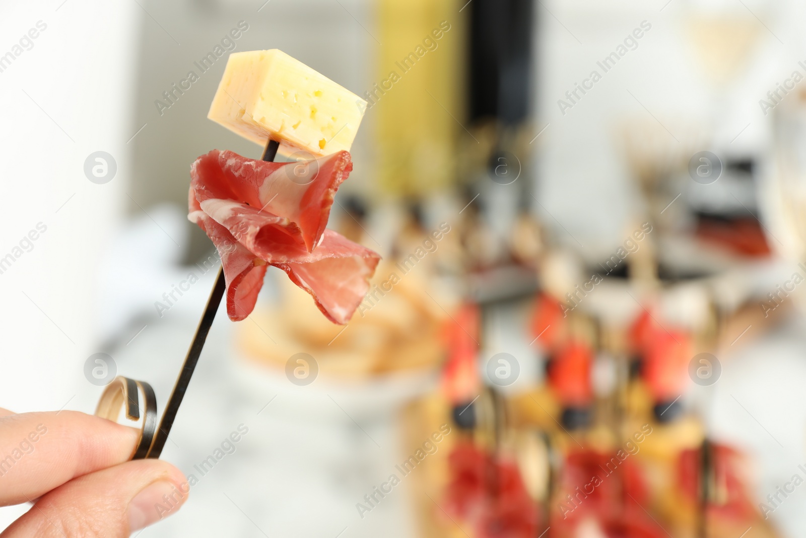 Photo of Woman holding tasty canape with cheese and prosciutto on table, closeup. Space for text