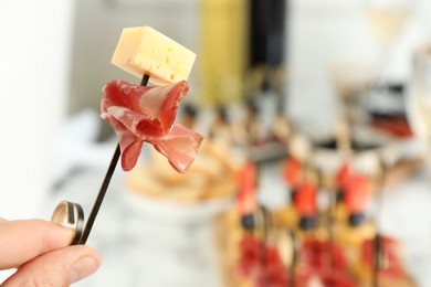 Photo of Woman holding tasty canape with cheese and prosciutto on table, closeup. Space for text