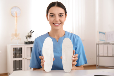 Photo of Young female orthopedist showing insoles in clinic