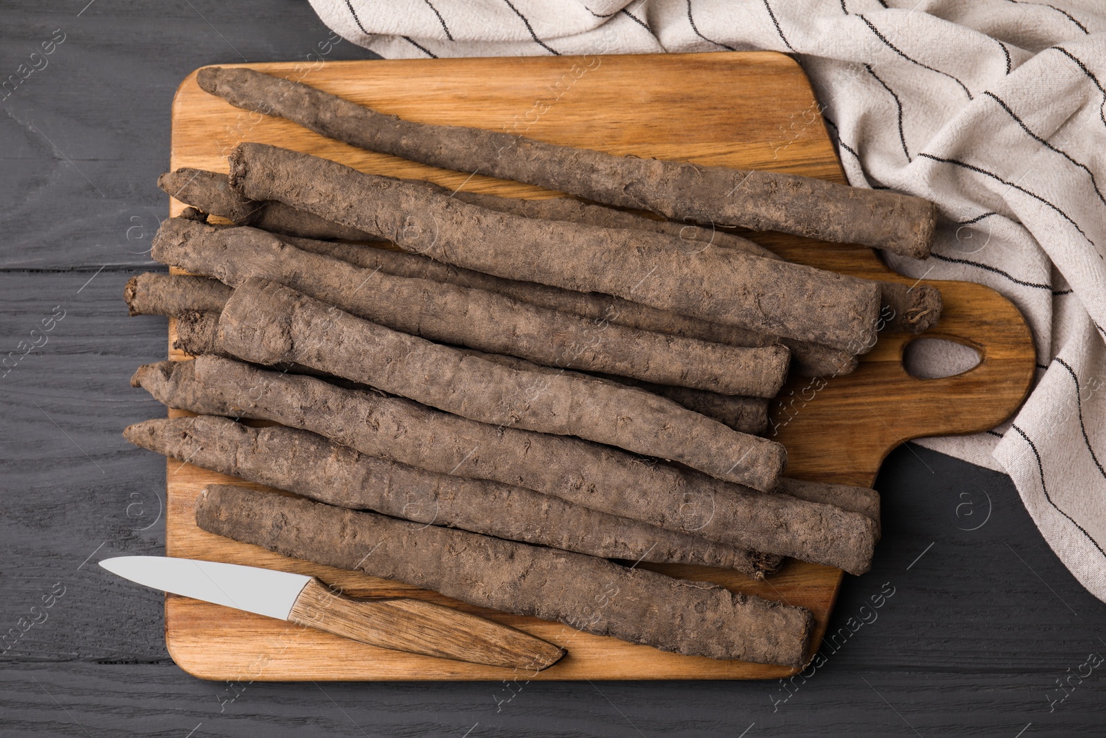 Photo of Raw salsify roots and knife on grey wooden table, top view