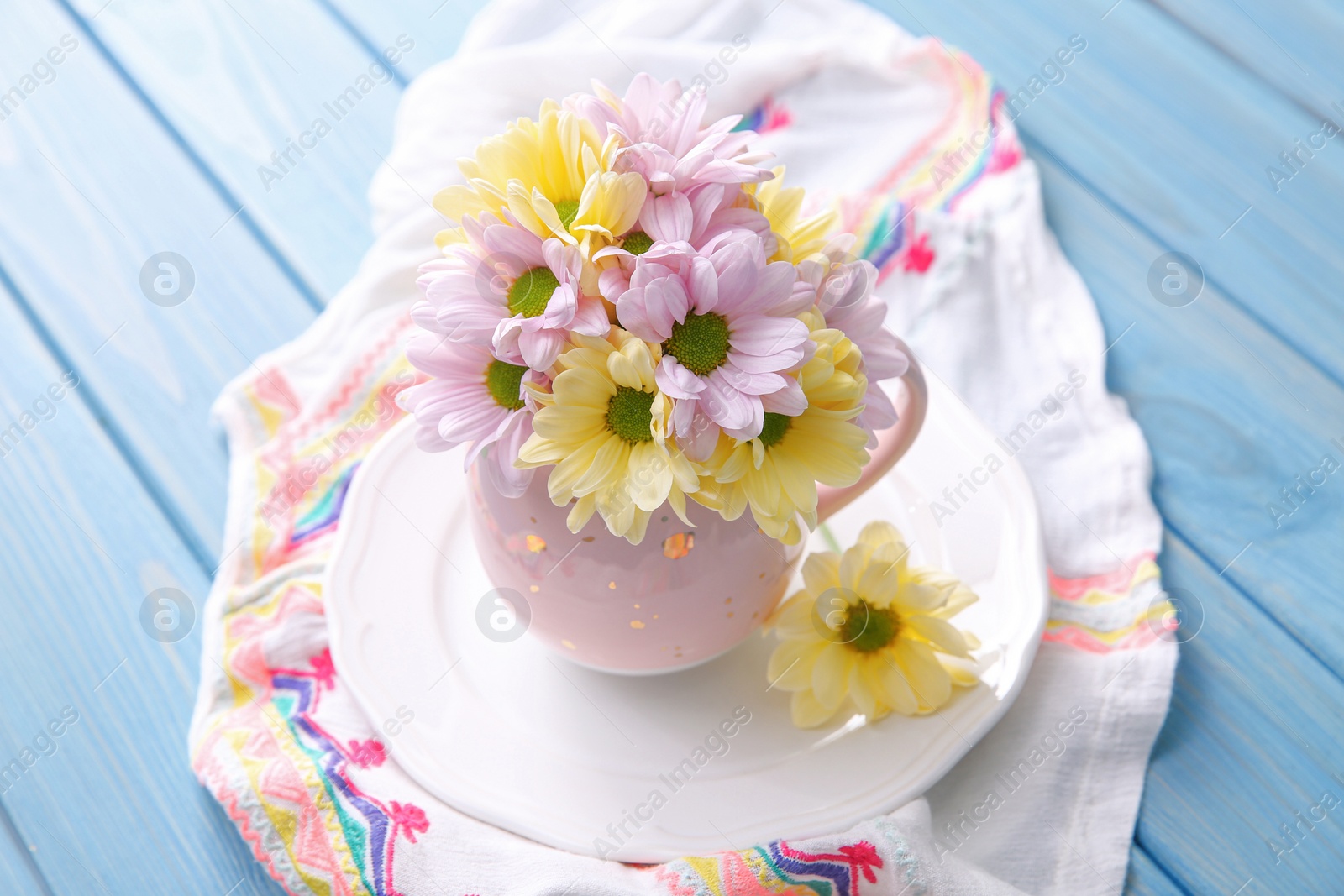 Photo of Bouquet of beautiful flowers in cup on light blue wooden table