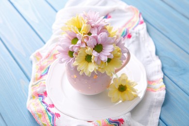 Photo of Bouquet of beautiful flowers in cup on light blue wooden table