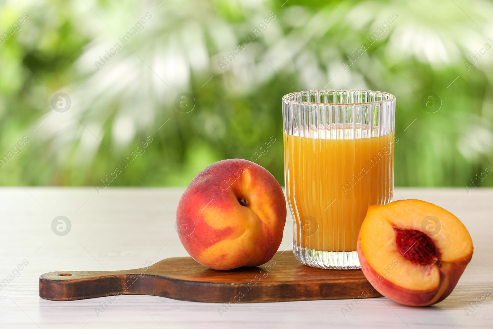 Photo of Glass of tasty peach juice and fresh fruits on white wooden table outdoors