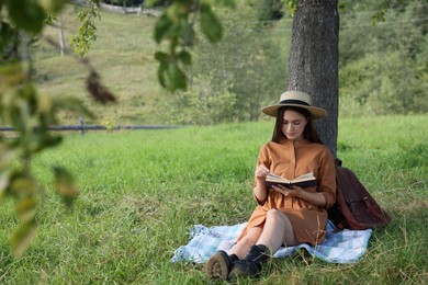 Photo of Young woman reading book under tree on meadow