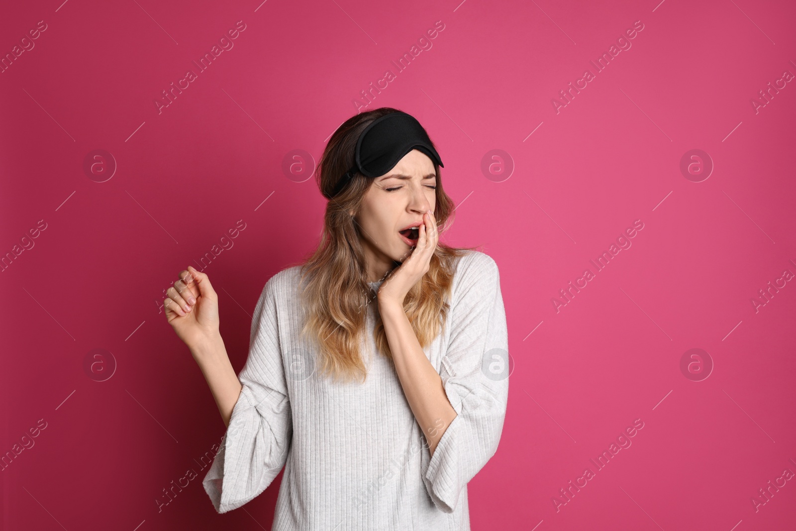 Photo of Young tired woman with sleeping mask yawning on pink background