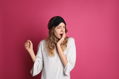 Photo of Young tired woman with sleeping mask yawning on pink background