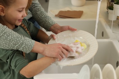 Photo of Mother and daughter washing plate above sink, closeup