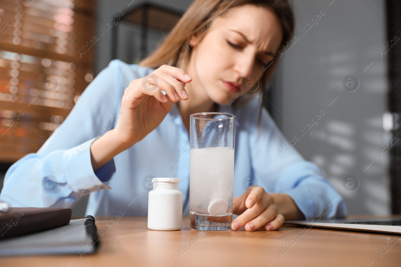Photo of Woman putting medicine for hangover into glass of water in office, focus on hands