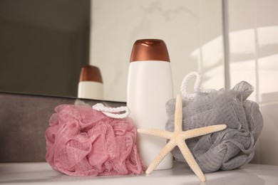 Photo of Colorful sponges between shower gel bottle and starfish on sink in bathroom