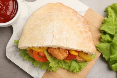 Photo of Delicious pita sandwich with fried fish, pepper, tomatoes and lettuce on light grey table, flat lay