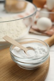 Photo of Baking powder in bowl and spoon on white table, closeup