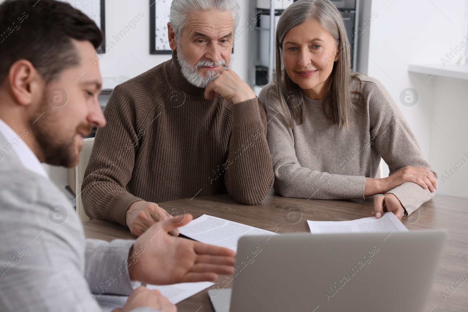 Photo of Elderly couple consulting insurance agent about pension plan at wooden table indoors