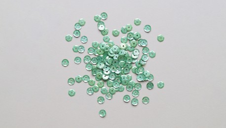 Pile of green sequins on light grey background, flat lay