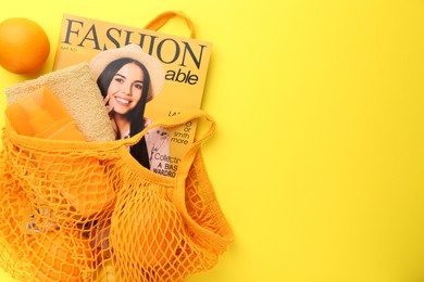 Photo of String bag with fresh oranges, fashion magazine and beach accessories on yellow background, top view. Space for text
