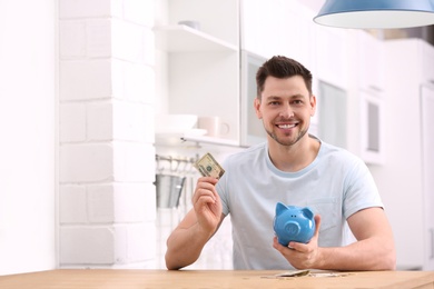 Photo of Man with piggy bank and money at home. Space for text