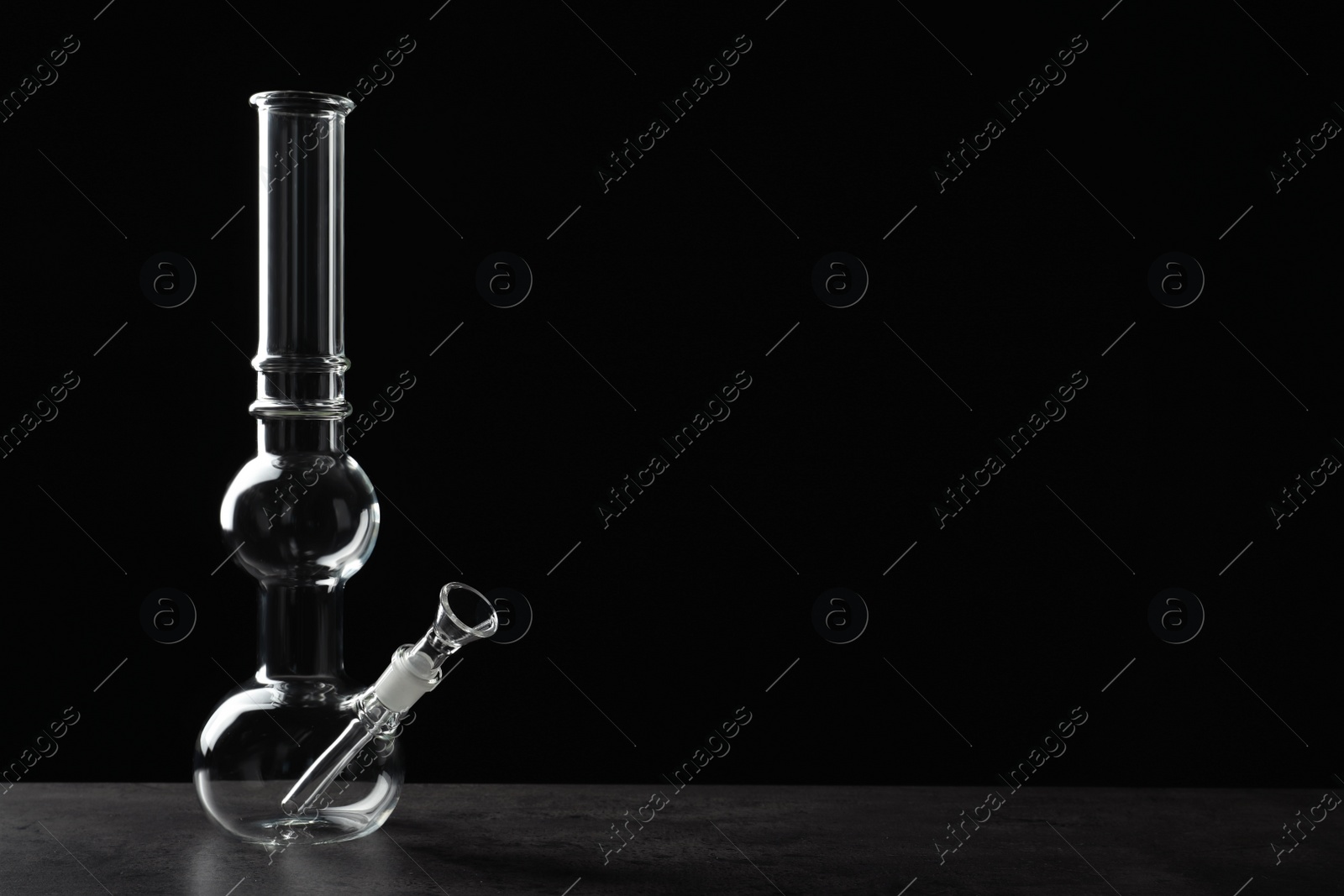 Photo of Glass bong on grey table against black background, space for text. Smoking device