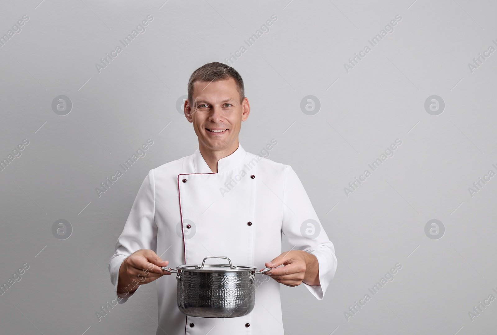 Photo of Happy male chef with cooking pot on light grey background