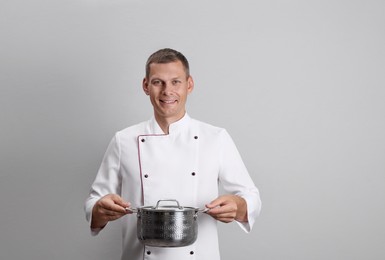 Happy male chef with cooking pot on light grey background