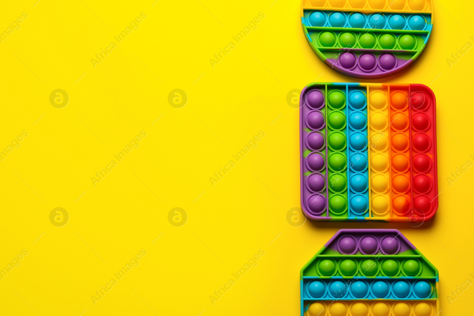 Photo of Rainbow pop it fidget toys on yellow background, flat lay. Space for text