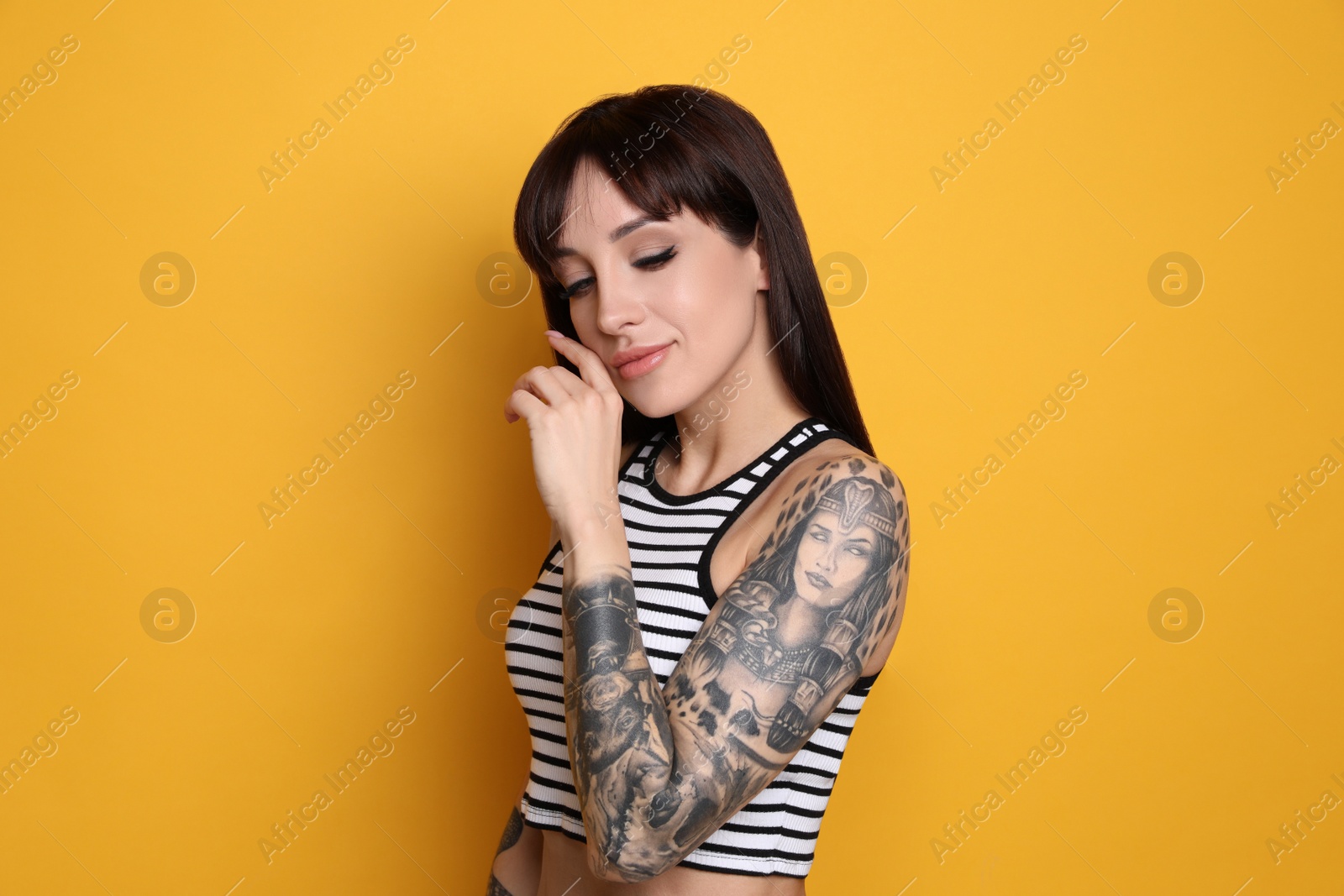 Photo of Beautiful woman with tattoos on arm against yellow background