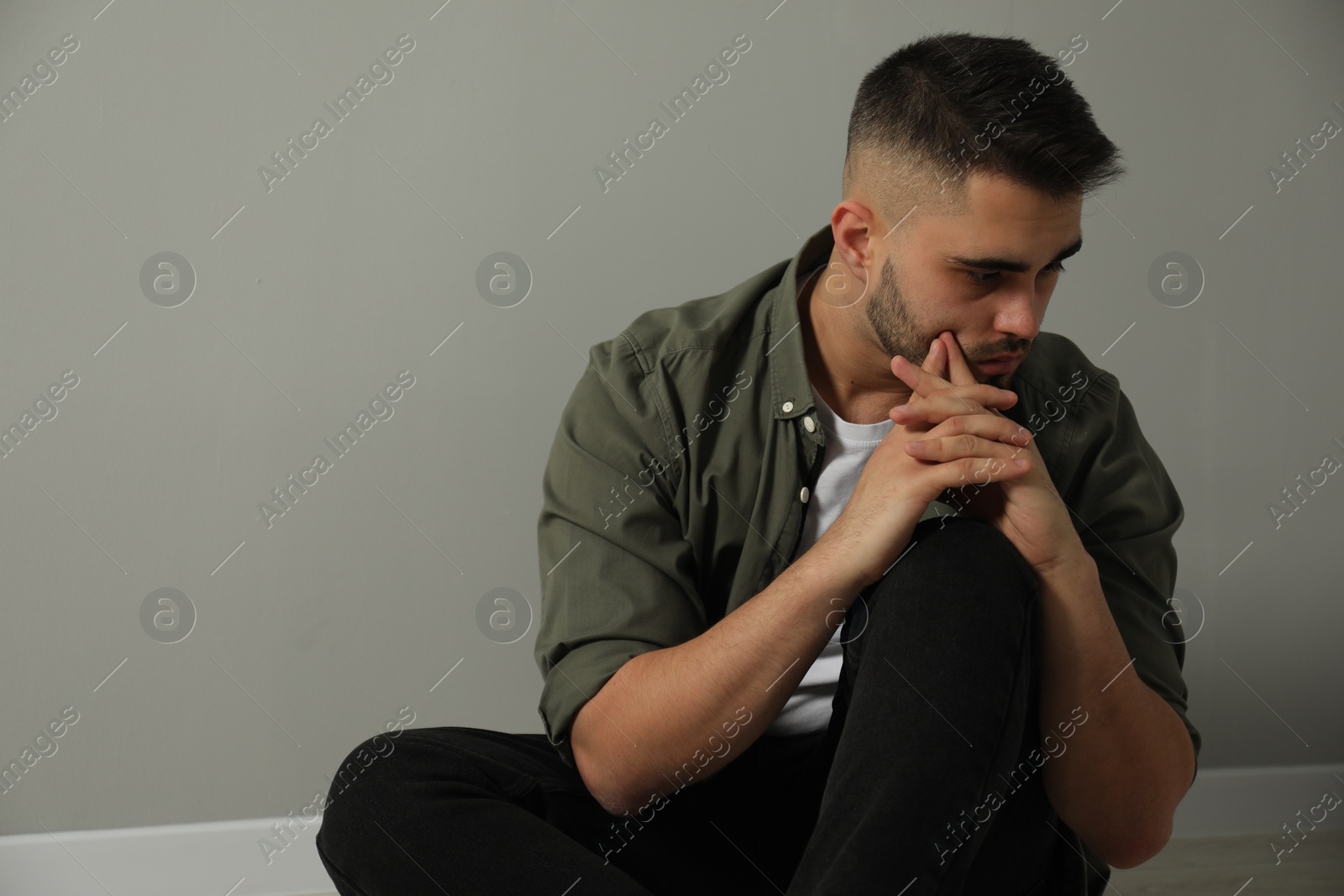 Photo of Sad man sitting near light grey wall. Space for text