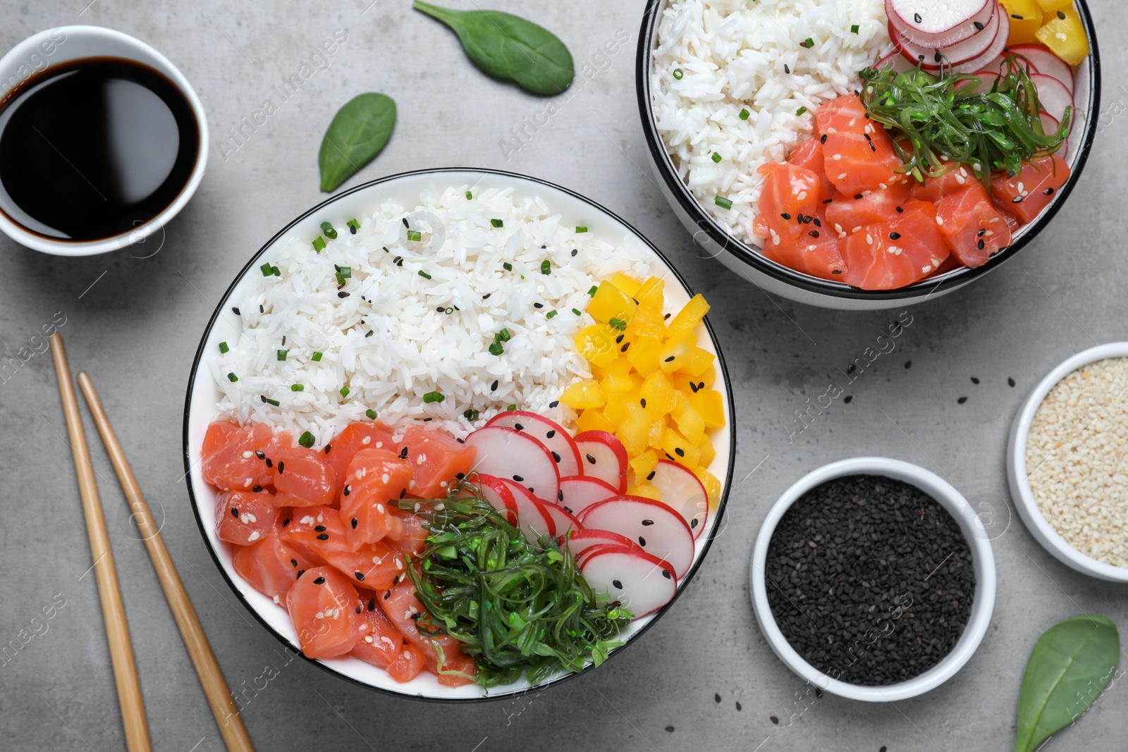 Photo of Delicious poke bowls with salmon and vegetables served on light grey table, flat lay